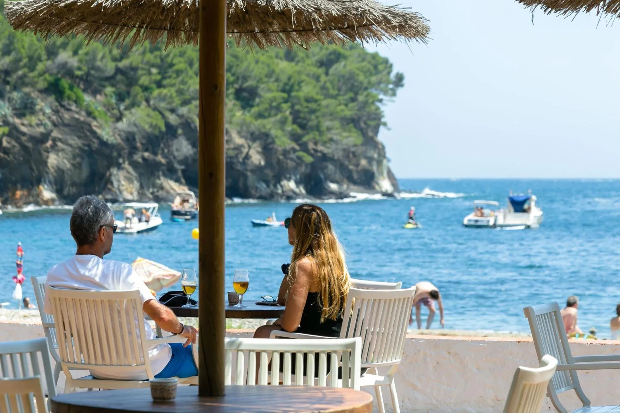 Deux personnes sont assises à une table en terrasse face à la mer.