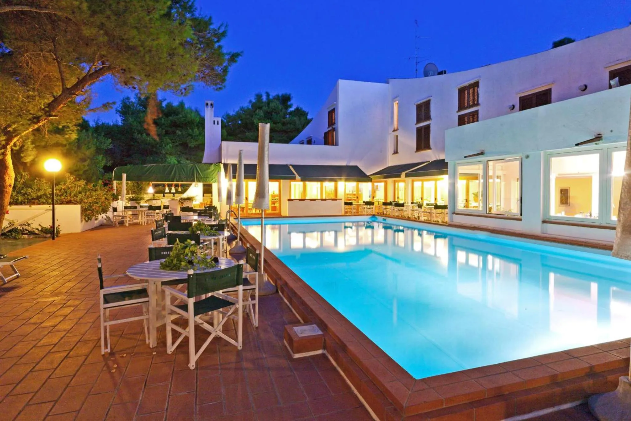 Une piscine illuminée au crépuscule avec des tables et des chaises.