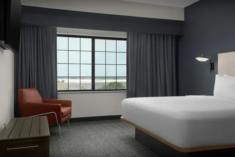 Une chambre d'hôtel moderne avec un lit et un fauteuil près d'une fenêtre.
