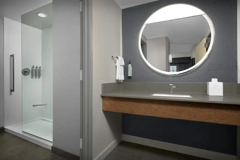 Une salle de bain moderne avec douche vitrée et grand miroir rond.