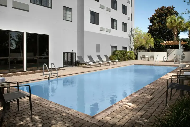 Piscine rectangulaire entourée d'une terrasse pavée et de chaises longues.
