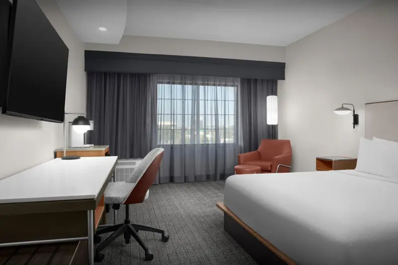 Une chambre d'hôtel lumineuse avec un bureau, un lit et un fauteuil.