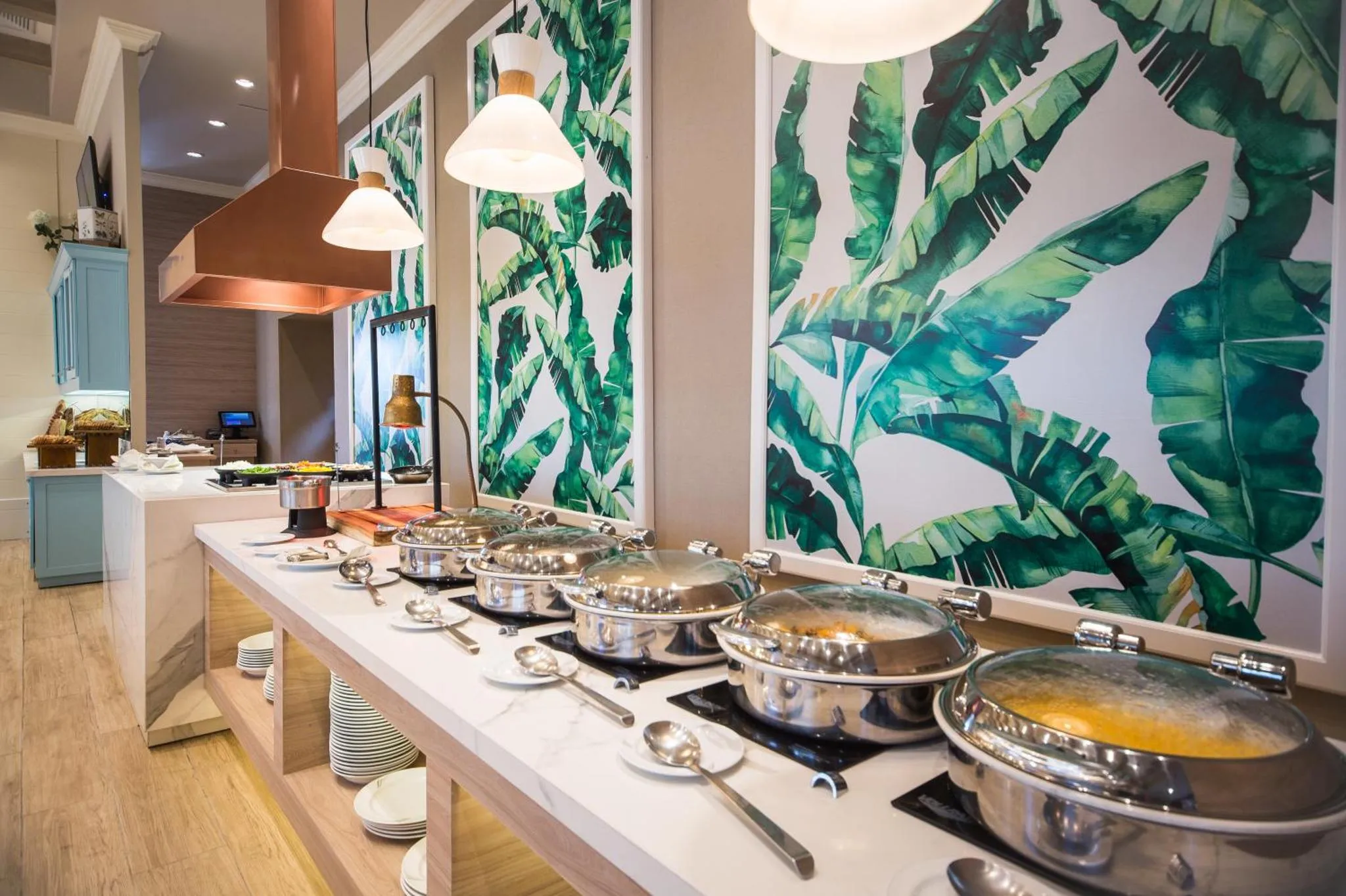 Un buffet propose une variété de plats chauds dans un espace lumineux et décoré de plantes.