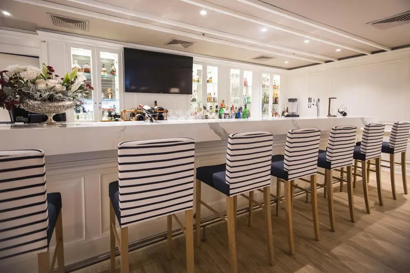 Un long comptoir de bar blanc avec des tabourets rayés est éclairé par des luminaires encastrés.