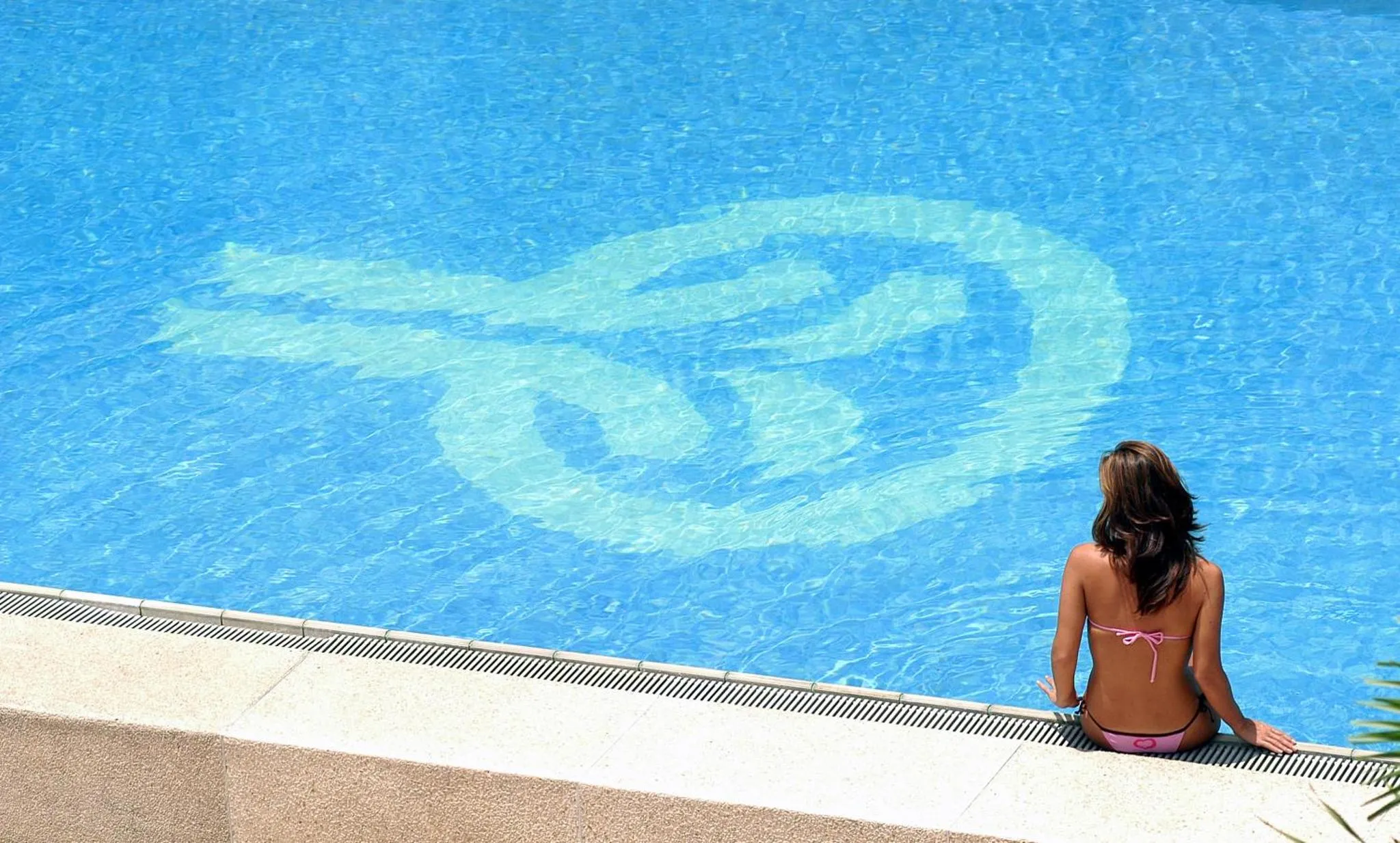 Une personne est assise au bord d'une piscine turquoise.