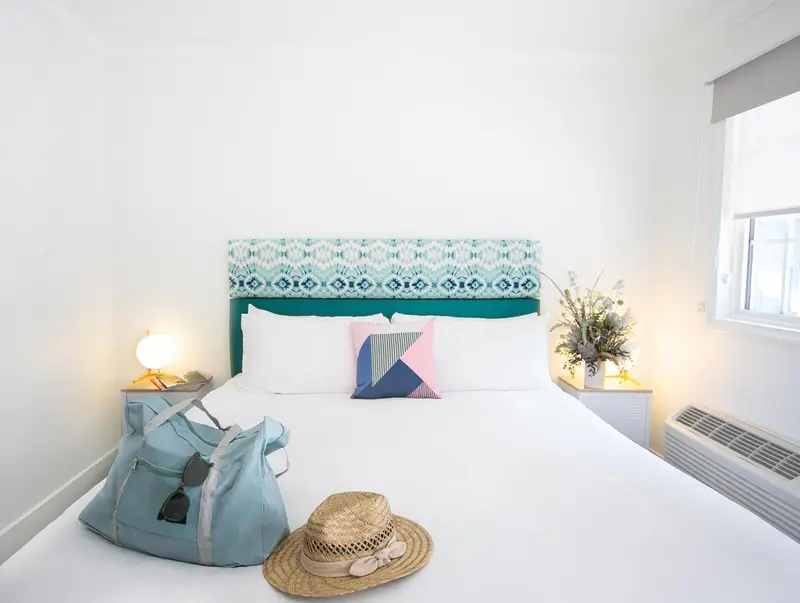 Une chambre lumineuse avec un grand lit recouvert d'une couette blanche et de coussins colorés.