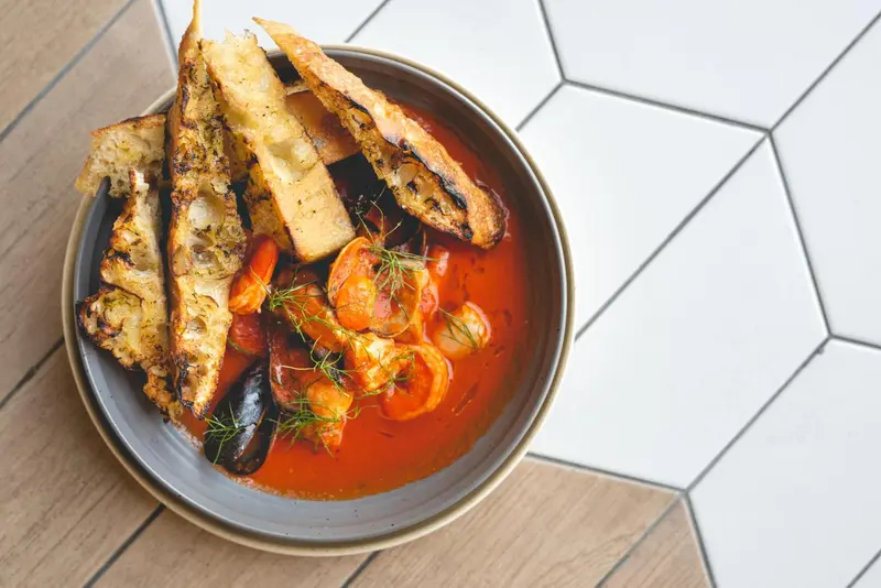 Assiette de crevettes et de pain grillé servi dans une sauce rouge.