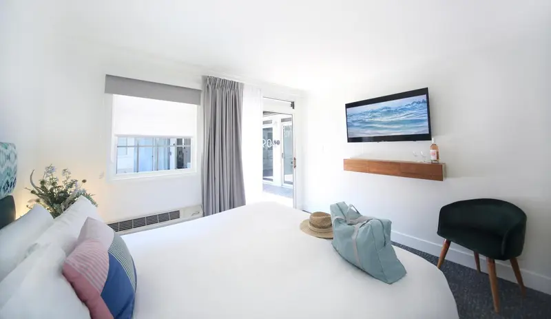 Chambre lumineuse avec un grand lit et un accès à une terrasse.