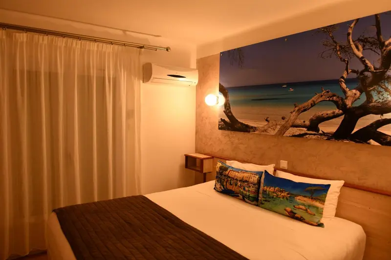 Une chambre lumineuse avec un grand lit et une décoration murale représentant un paysage marin.