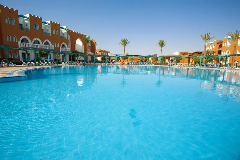 Une grande piscine turquoise bordée de transats devant un bâtiment aux couleurs vives.
