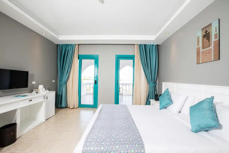 Chambre lumineuse avec un lit blanc et des rideaux turquoise.