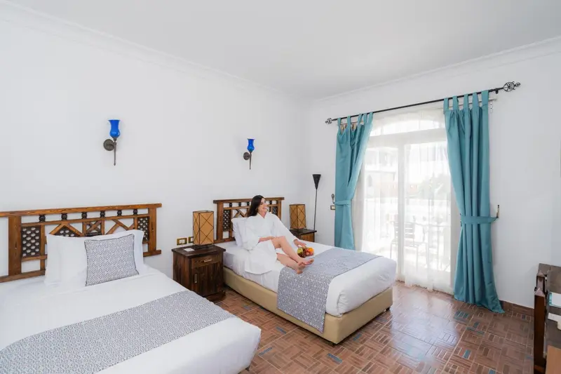 Chambre lumineuse avec deux lits simples et rideaux bleus.