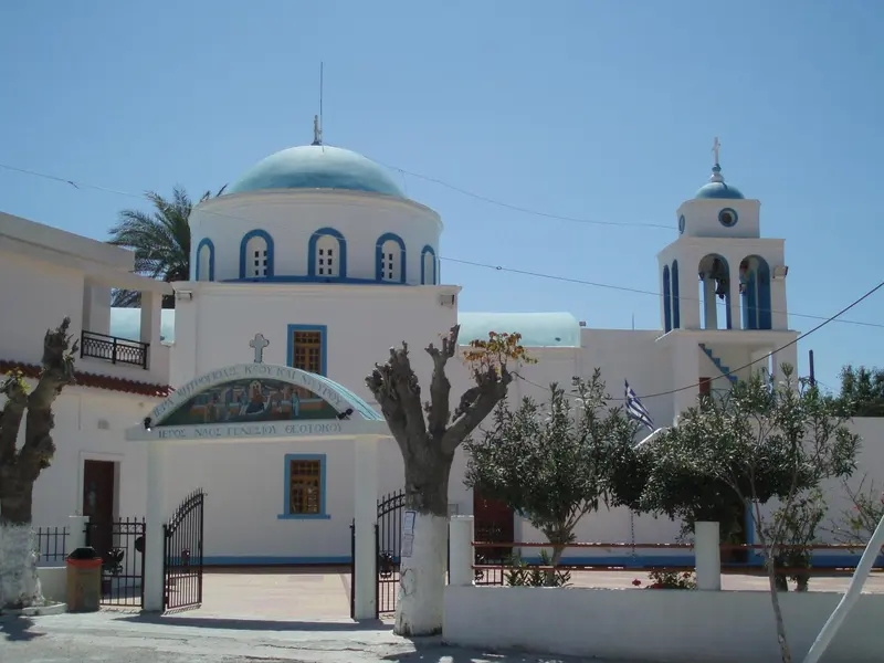 Bâtiment blanc avec dôme bleu et clocher, entouré de végétation et d'une clôture.