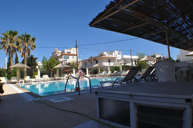 Transats et parasols bordent une piscine ensoleillée devant un bâtiment blanc.