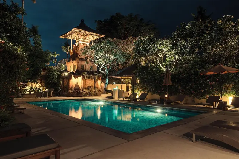 Piscine illuminée au crépuscule avec bâtiment traditionnel en arrière-plan.