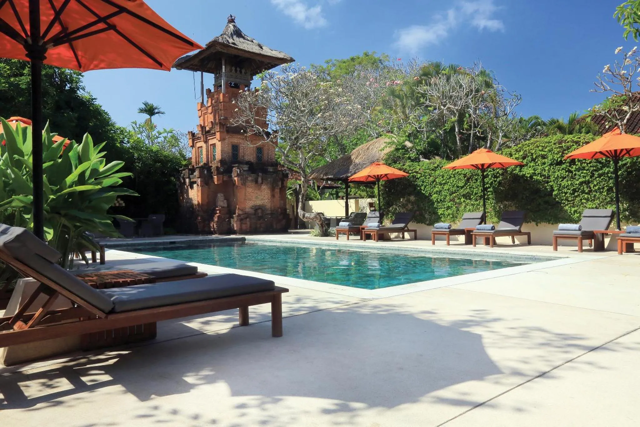 Transats et parasols bordent une piscine turquoise dans un cadre tropical.