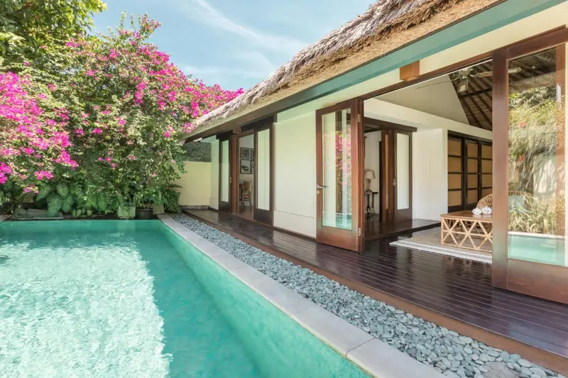 Une piscine turquoise bordée d'une terrasse en bois devant une habitation.