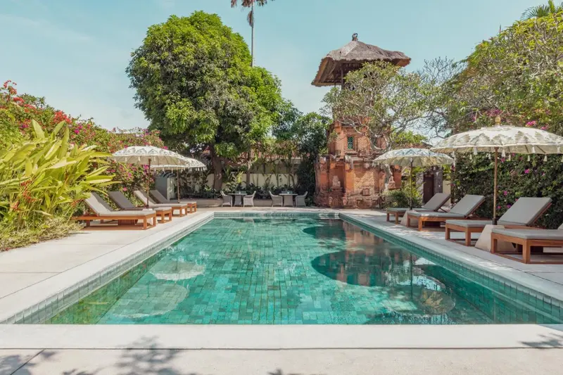 Une piscine rectangulaire turquoise bordée de transats sous des parasols.