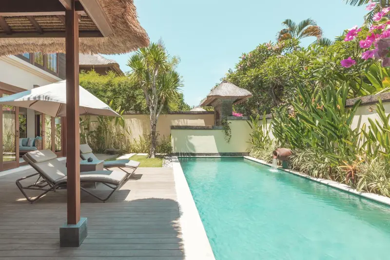 Terrasse avec transats et piscine rectangulaire dans un jardin tropical.