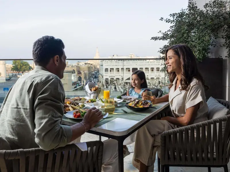 Une famille prend son repas sur une terrasse ensoleillée avec vue sur une ville historique.