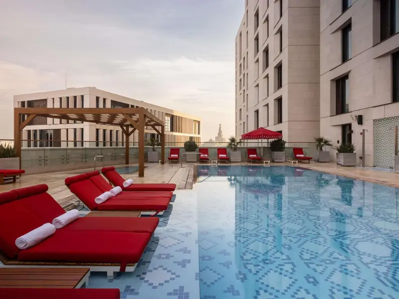 Transats rouges disposés autour d'une piscine rectangulaire dans un espace extérieur.
