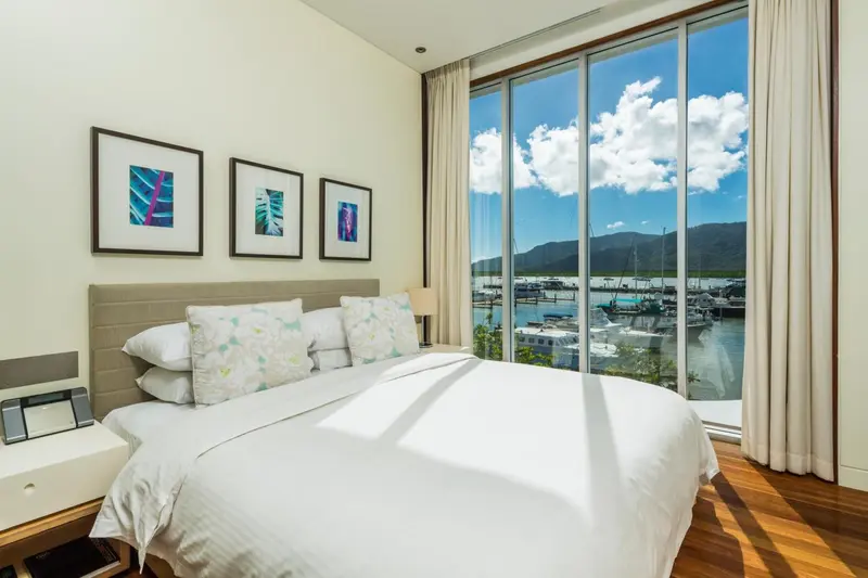 Une chambre lumineuse avec un grand lit face à une baie vitrée donnant sur un port de plaisance.