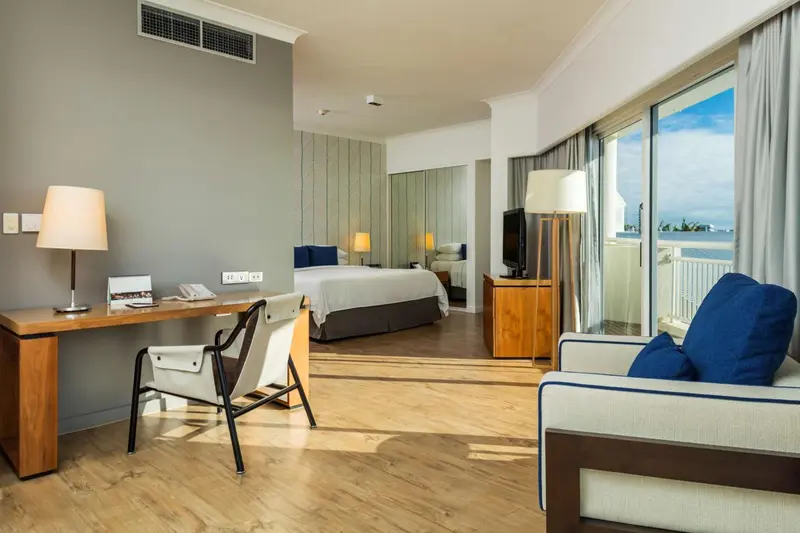 Une chambre lumineuse avec un bureau, un lit et un coin salon donnant sur une vue dégagée.