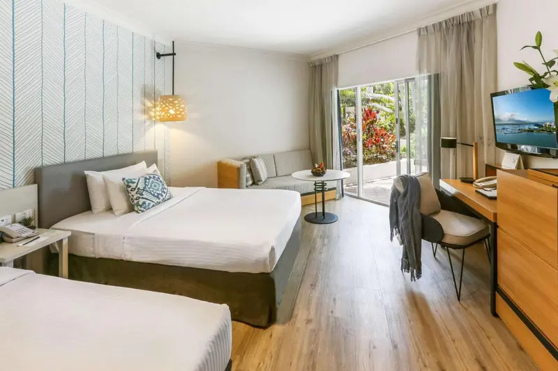 Une chambre lumineuse avec un lit double et un coin salon donnant sur une terrasse.