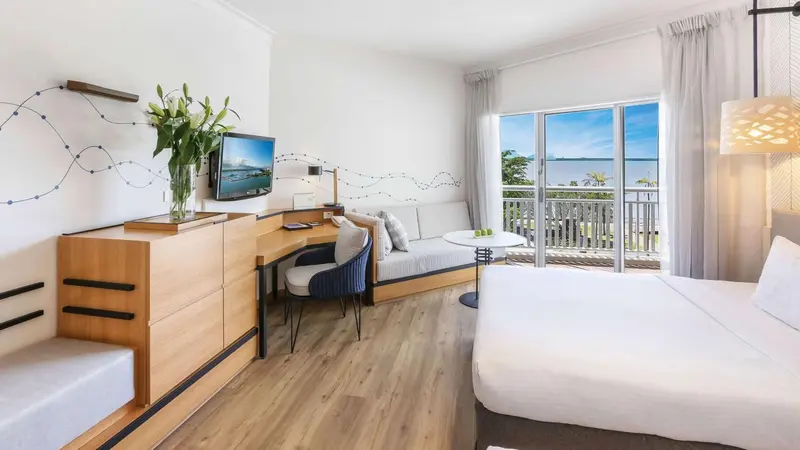 Une chambre lumineuse avec un lit, un coin salon et un balcon donnant sur la mer.