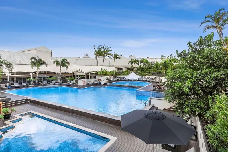 Vue aérienne d'une piscine d'hôtel entourée de chaises longues et de végétation tropicale.
