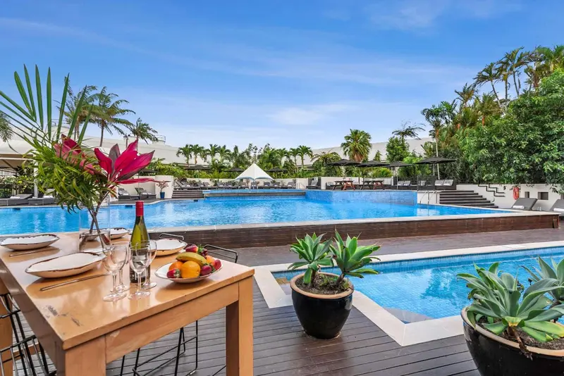 Une table dressée près d'une piscine ensoleillée avec une végétation luxuriante en arrière-plan.