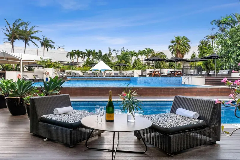 Deux fauteuils et une table basse avec une bouteille de champagne près d'une piscine.
