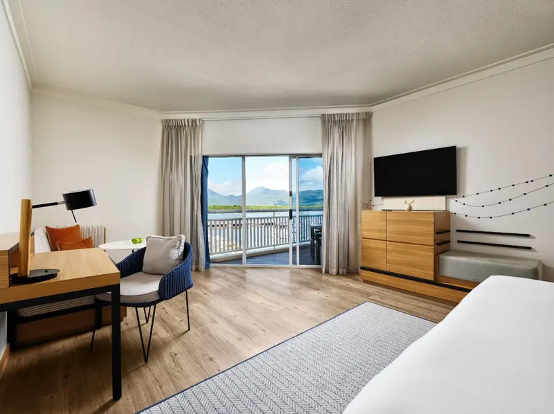 Une chambre lumineuse avec un bureau, un fauteuil et un accès à un balcon avec vue sur la mer.