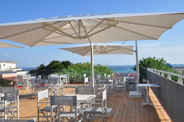 Terrasse ombragée avec tables et chaises donnant sur la mer.