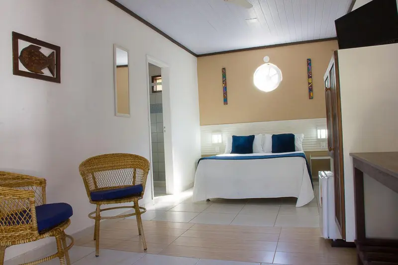 Une chambre lumineuse avec un lit double et un coin salon en rotin.