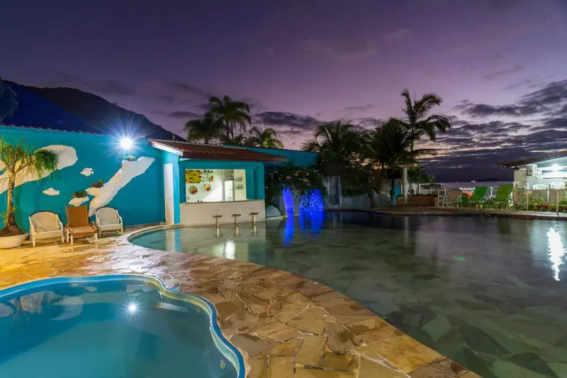Piscine illuminée avec bar et mobilier de jardin au crépuscule.