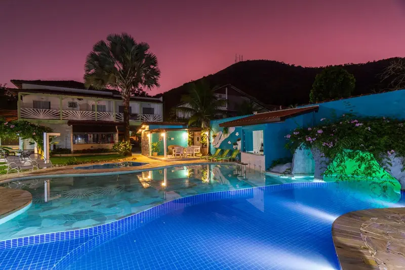 Piscine illuminée devant un bâtiment coloré au coucher du soleil.
