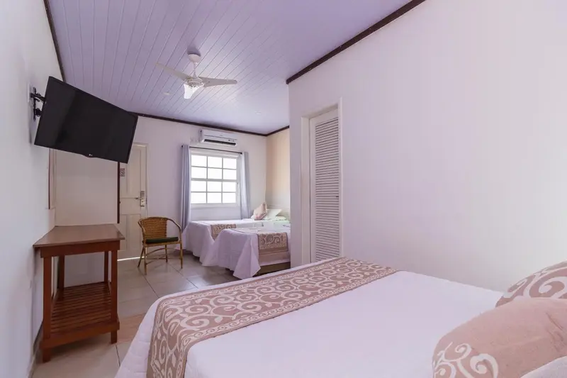 Une chambre lumineuse avec deux lits et un ventilateur au plafond.