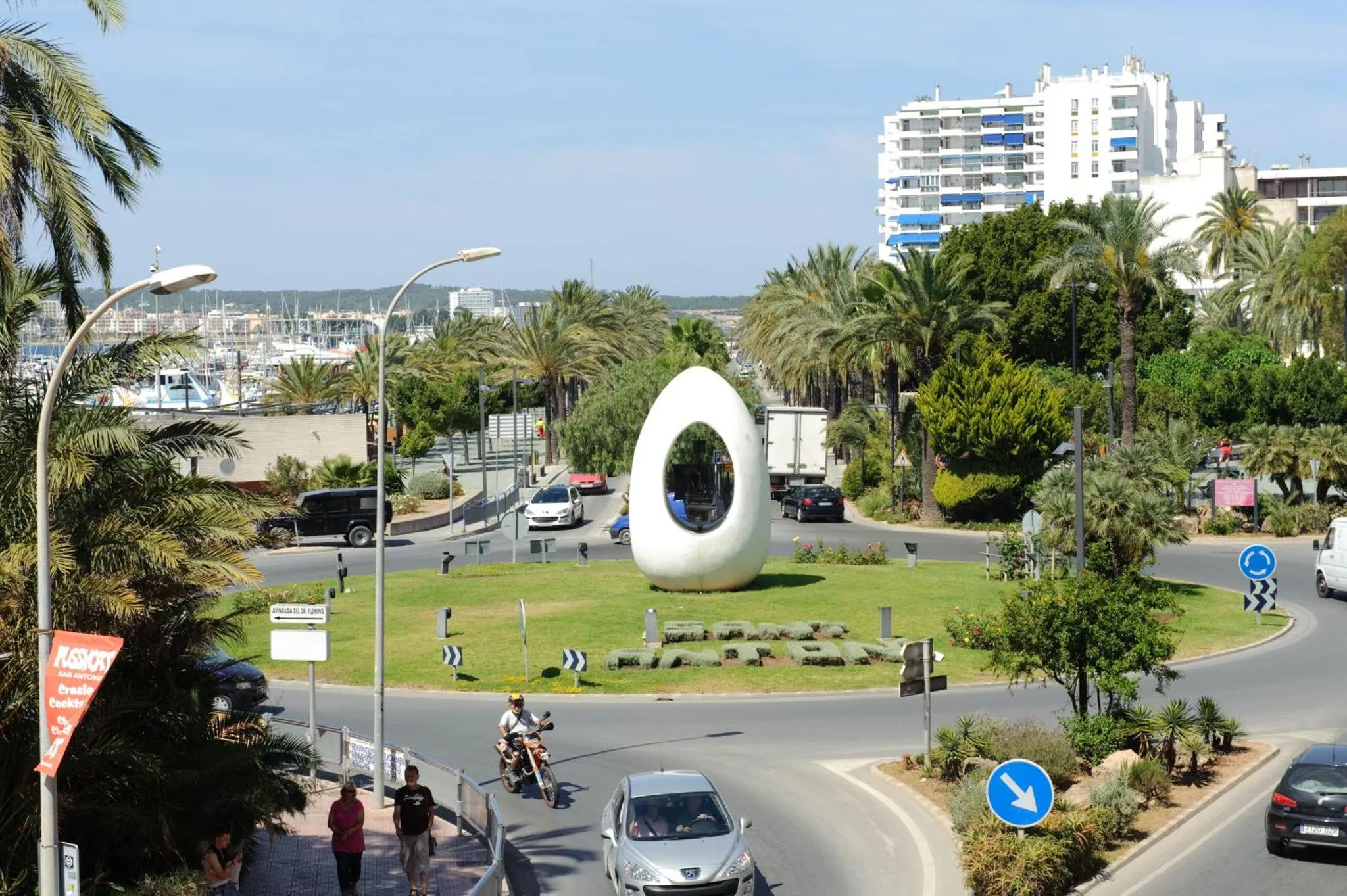 Une sculpture blanche moderne orne un rond-point verdoyant en bord de mer.