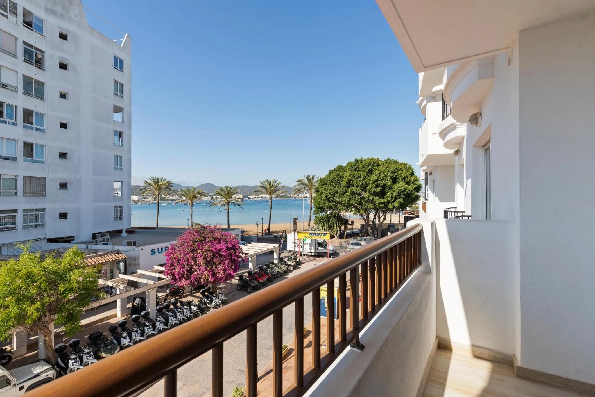 Vue d'un balcon avec une rambarde blanche donnant sur la mer et la végétation.