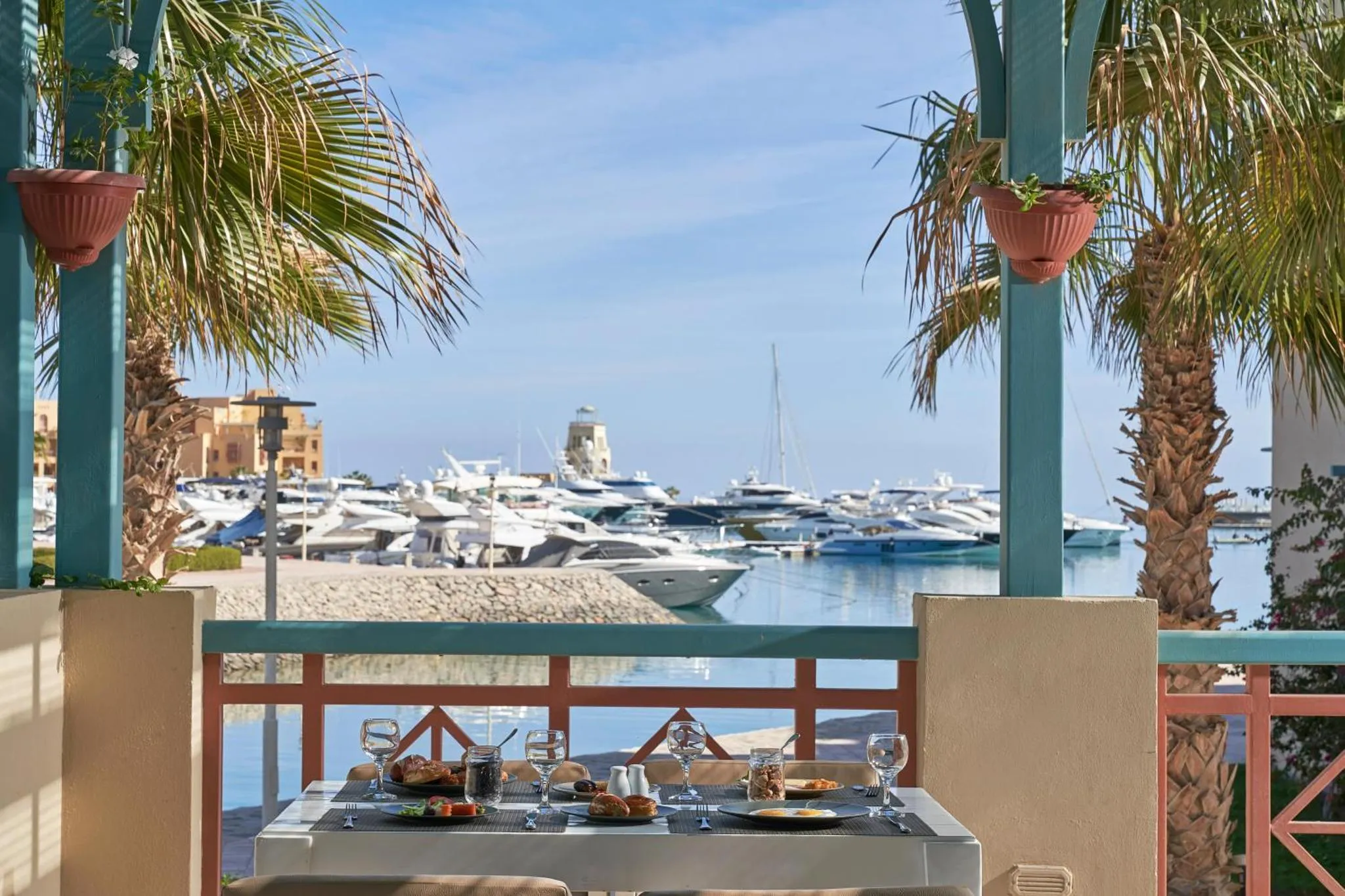 Une table est dressée pour un repas en extérieur avec vue sur un port de plaisance.