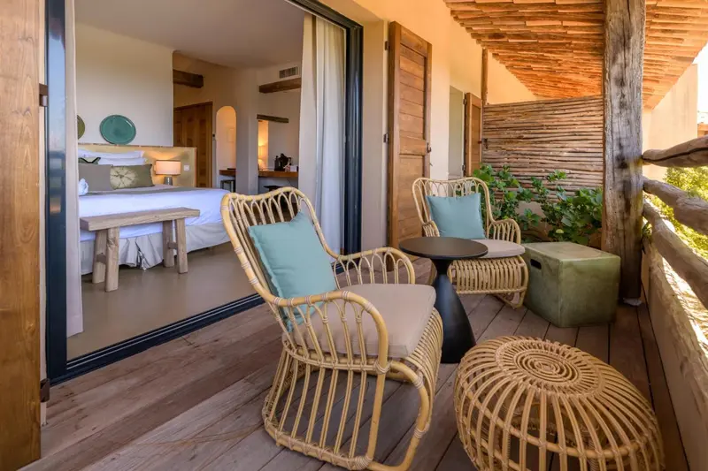Terrasse aménagée avec mobilier en rotin donnant sur une chambre lumineuse.