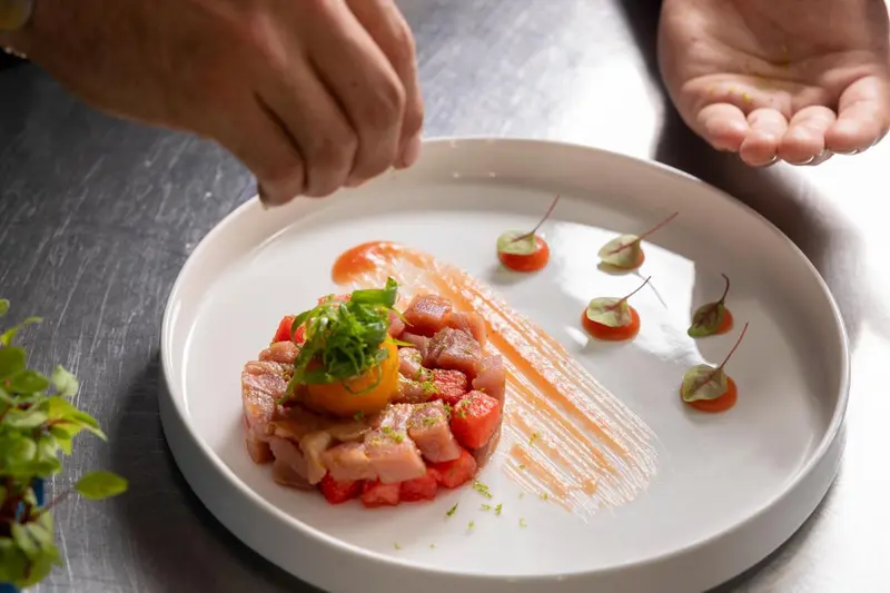 Une assiette de poisson cru est décorée avec des herbes et des sauces colorées.