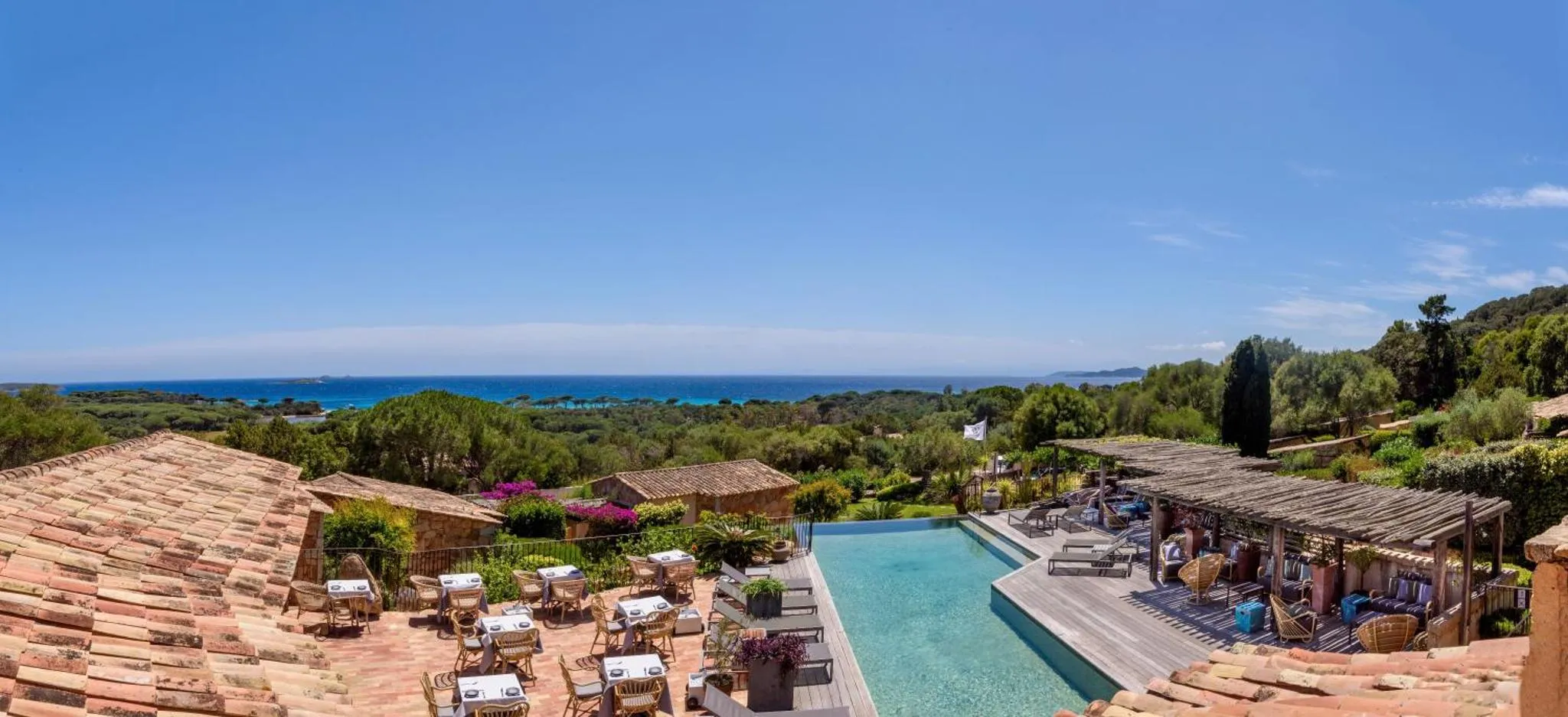 Terrasse ombragée avec tables et chaises donnant sur une piscine et la mer.