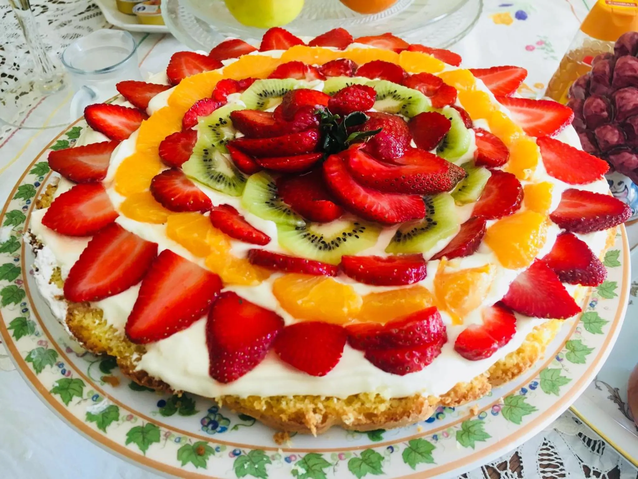 Une grande tarte aux fruits frais décorée en forme de fleur est présentée sur une assiette.