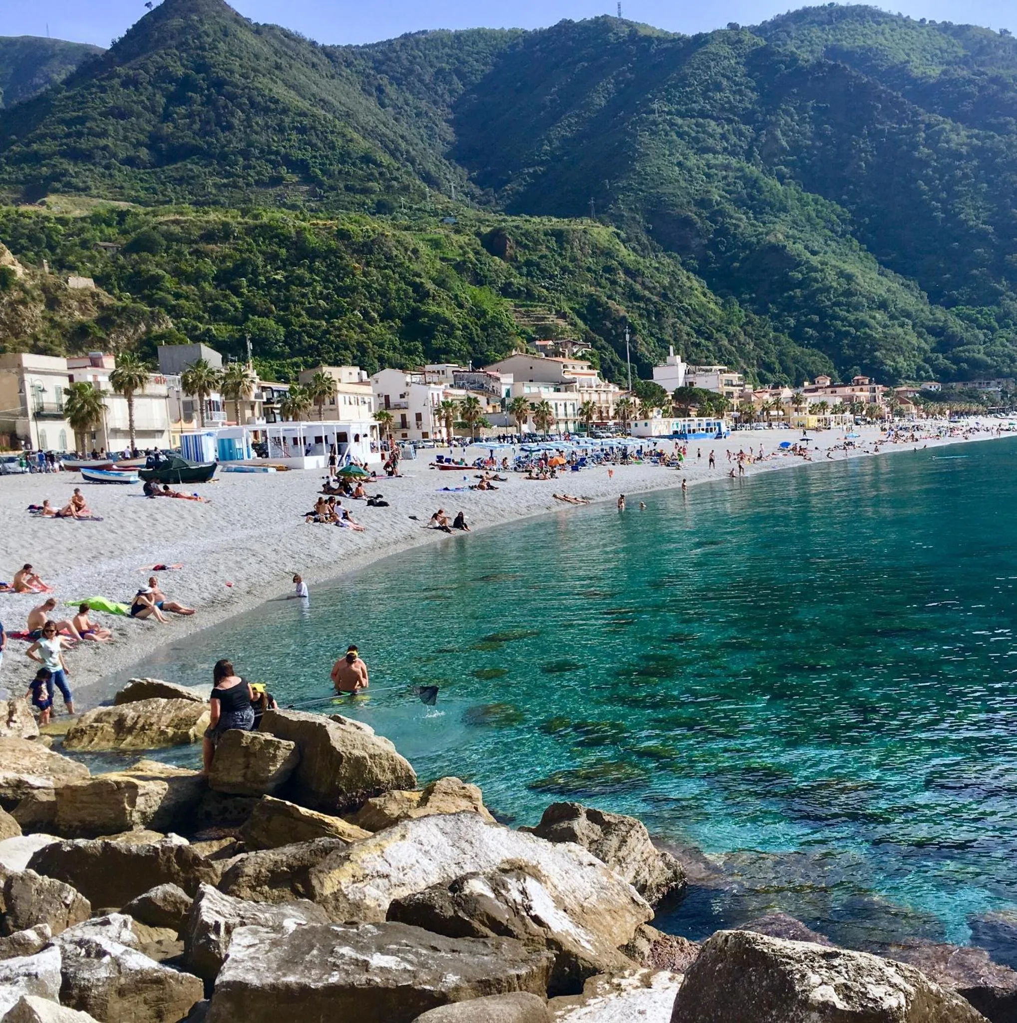 Une plage de galets bordée d'une eau turquoise, avec des personnes se baignant et se relaxant au soleil.