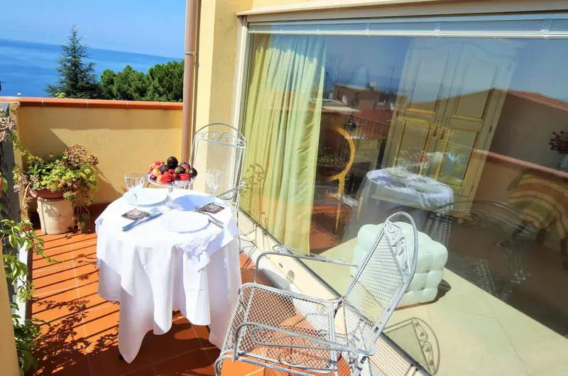 Une table est dressée sur une terrasse ensoleillée avec vue sur la mer.