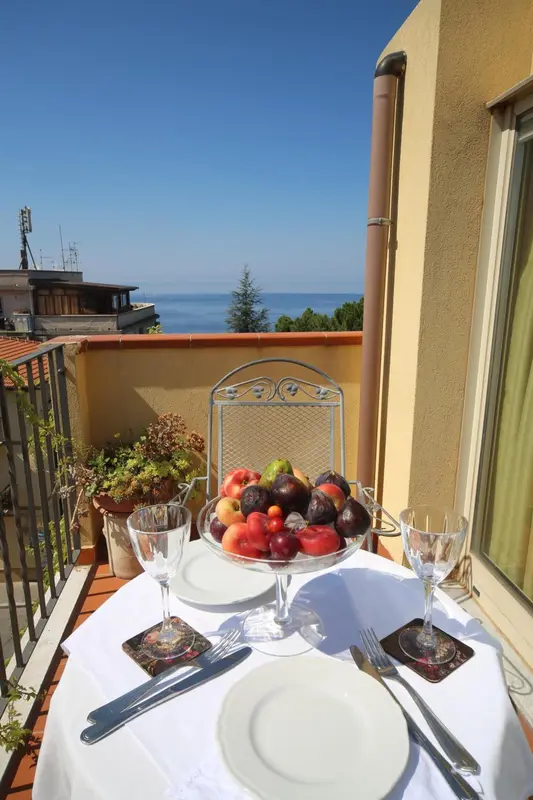 Une table dressée avec des fruits et des couverts sur un balcon ensoleillé.