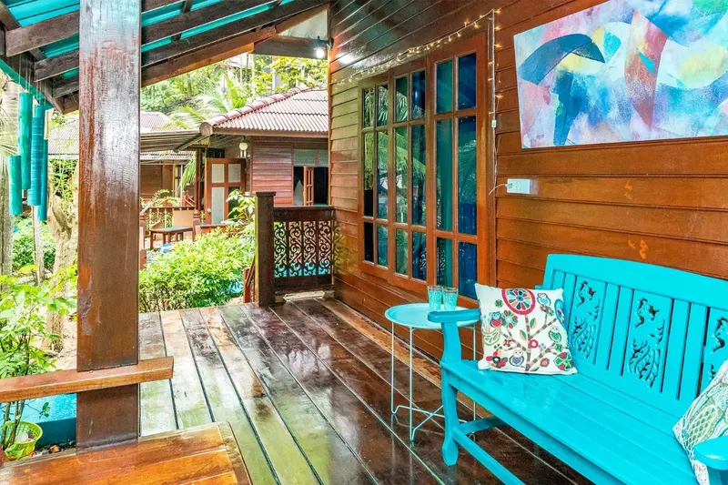 Terrasse en bois avec banc bleu et végétation luxuriante.