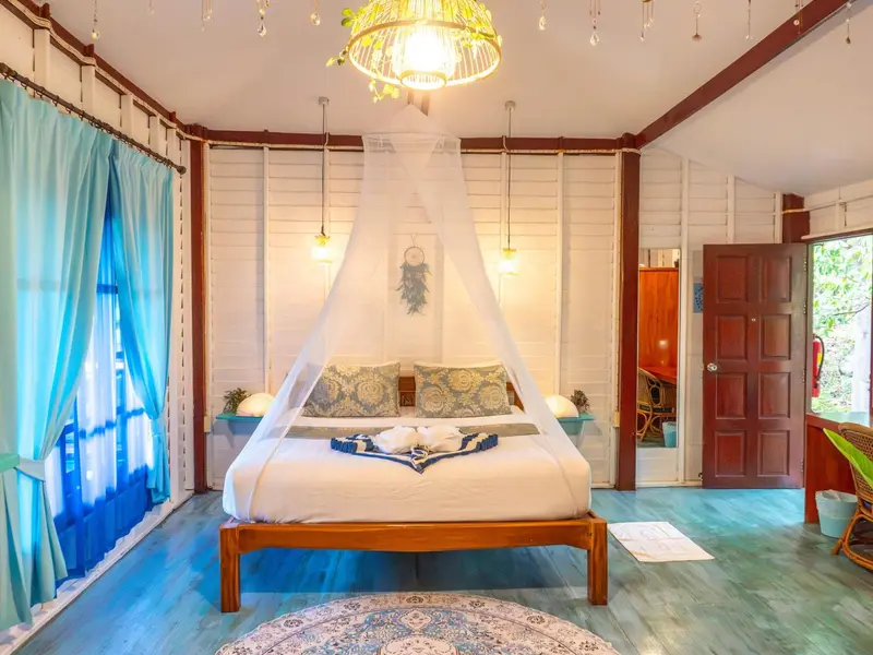 Une chambre lumineuse avec un grand lit à baldaquin et des rideaux turquoise.